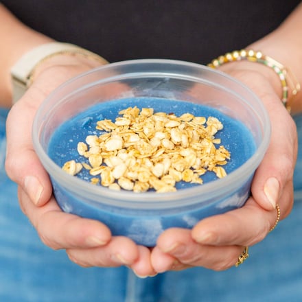 Person holding blue smoothie bowl with granola